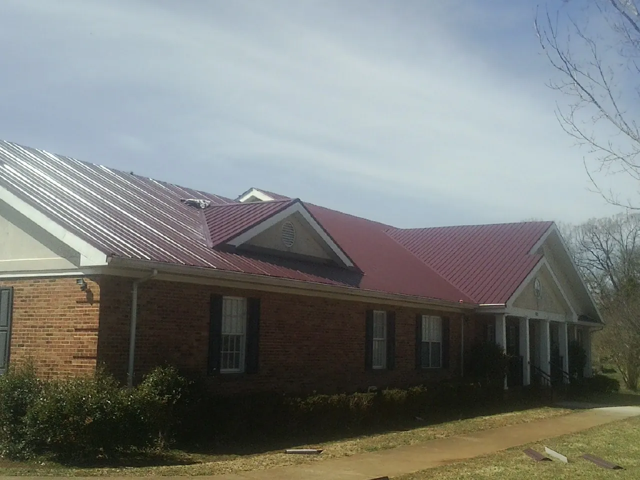 Red metal roof with gabled entries on a long brick building, from a Hail Damage Roof Repair job in Spragueville