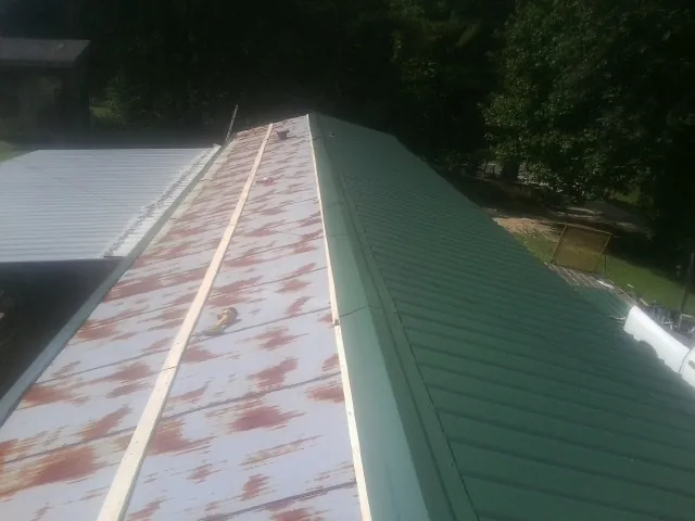Old rusted panels beside newly installed green metal roofing — Wind Damage Roof Repair by Roofing Brothers in Spragueville
