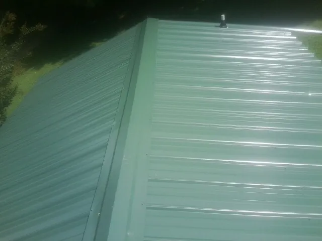New green metal panels meeting at the ridge of a roof — Flat Roof Repair work by our crew in Spragueville