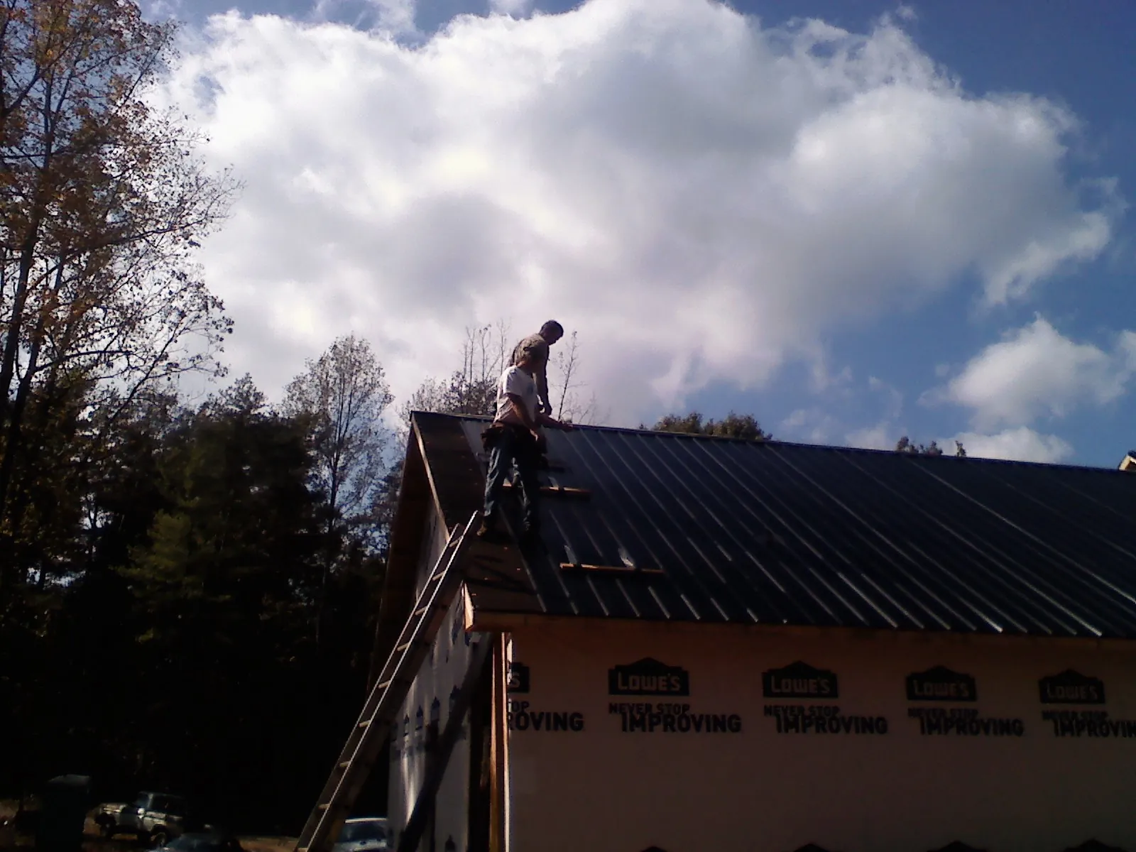 Roofer fastening dark metal panels high against a cloudy sky, from a Roof Inspection job in Spragueville