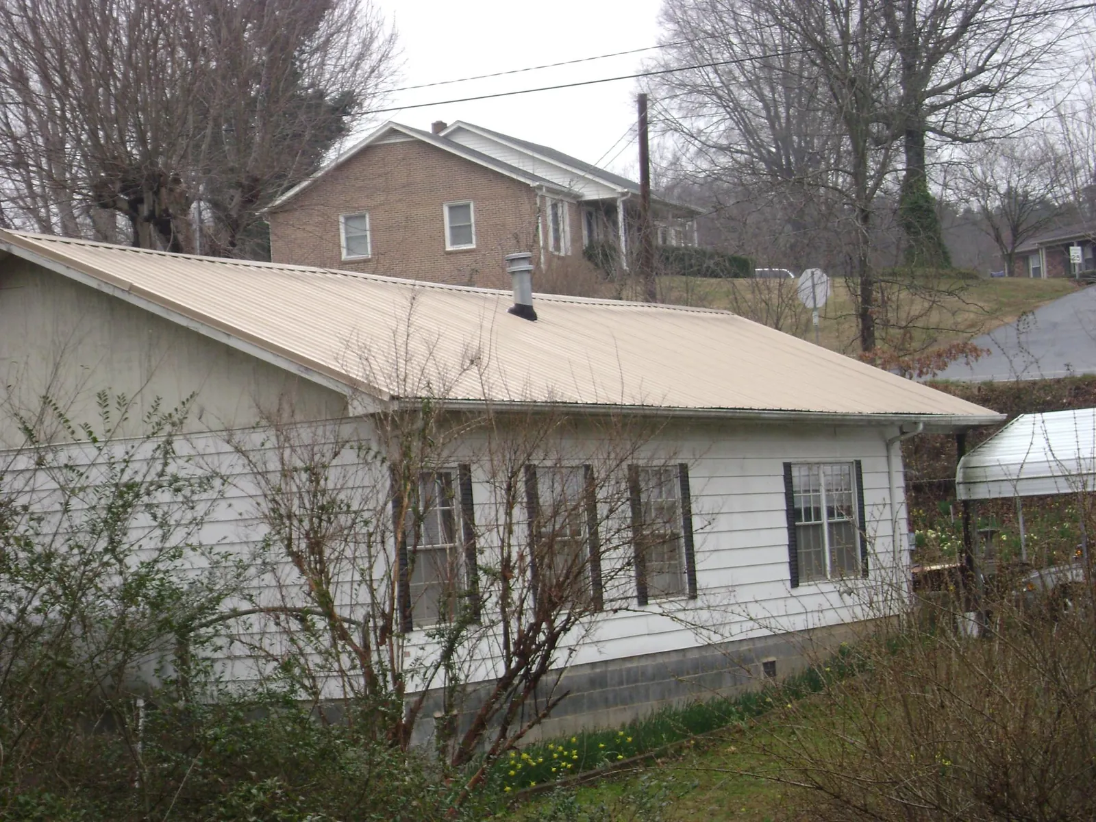 Tan metal roof on a white sided house set into a hillside — Commercial Roofing by Roofing Brothers in Spragueville