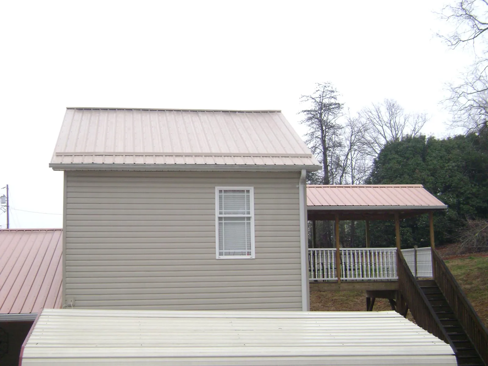 Tan metal roofs on a two story addition and attached porch, from a Roof Replacement job in Spragueville